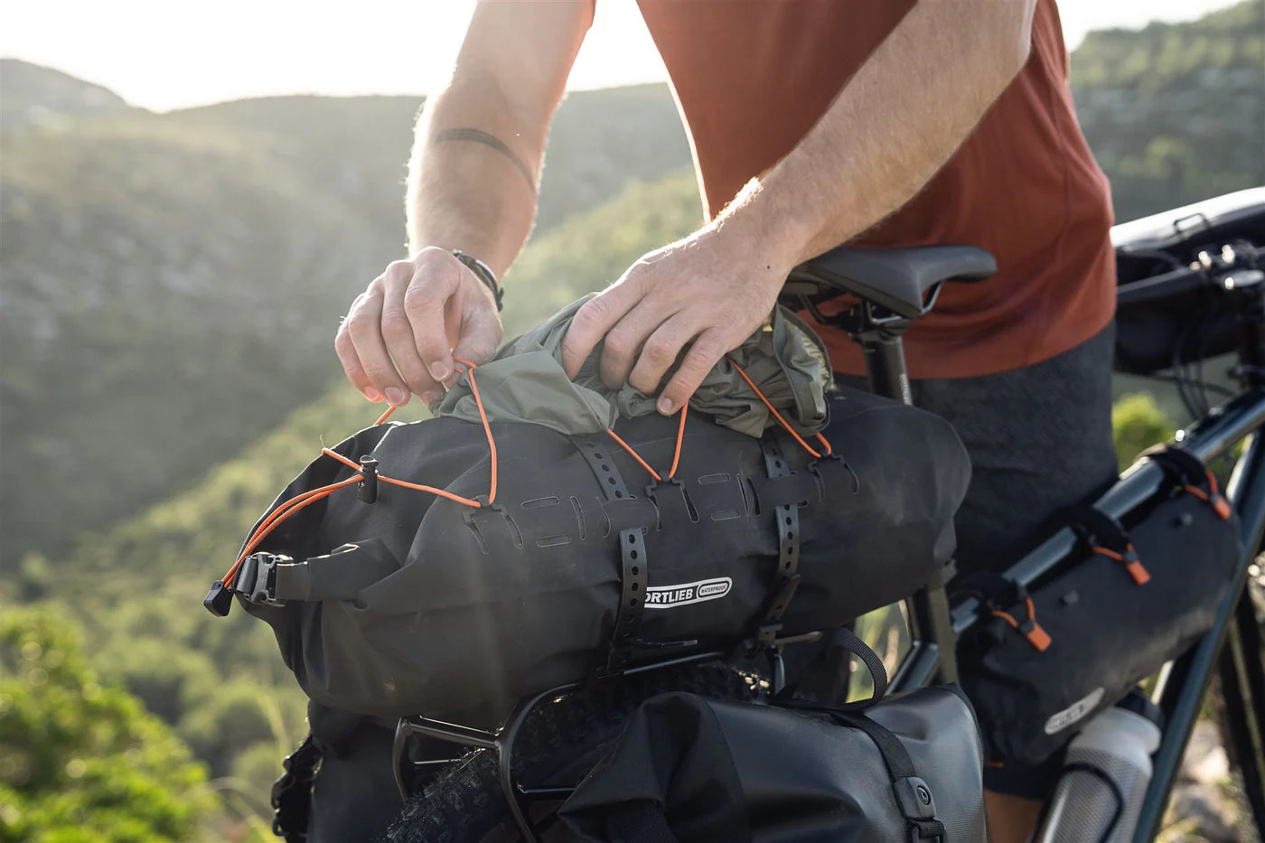 Person securing the Ortlieb Dry Pack bag on a bicycle with a scenic background