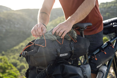 Person securing the Ortlieb Dry Pack bag on a bicycle with a scenic background